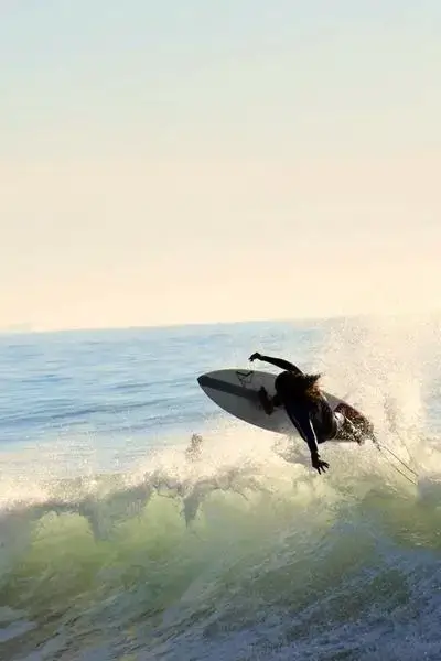 A lone surfer in silhouette launching off the lip of a translucent green wave under sunlight at Anza beach, agadir morocco surf