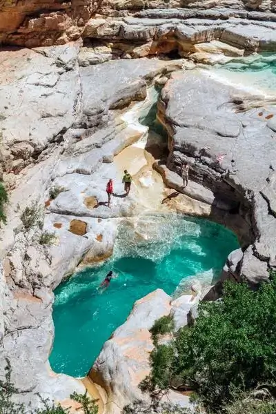 Adventurers paddle along a narrow limestone canyon pool with emerald-blue water beneath sunlit cliffs in agadir morocco surf