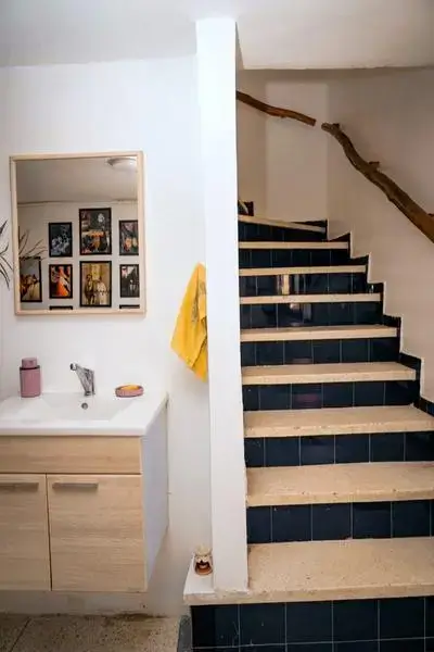 Compact washbasin with light wood cabinetry, chrome faucet, pink soap dispenser, yellow hand towel, and navy-blue tiled staircase reflecting agadir morocco surf style