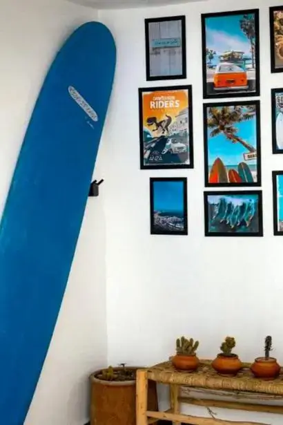 A bright seaside-inspired corner with a sky-blue surfboard and framed surf prints above a bench of terracotta potted succulents, agadir morocco surf decor