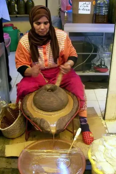 Local artisan turning a stone grinder to press roasted argan kernels into paste in a small stall at agadir morocco surf beach town
