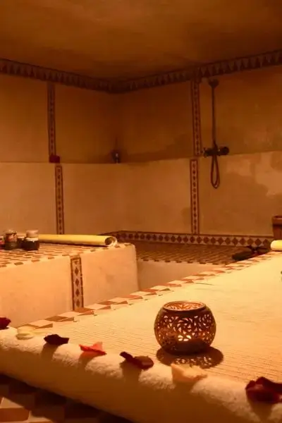 Amber-lit traditional hammam interior with zellige mosaic tiles, rose petals and spa jars in agadir morocco surf setting