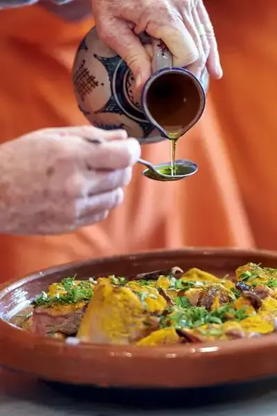 agadir morocco surf scene with hands drizzling olive oil onto fresh fish in a terracotta bowl