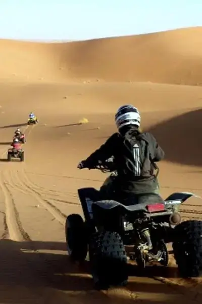 A line of all-terrain quad bikes carving tracks through rolling golden dunes under a clear blue sky in Anza, invoking agadir morocco surf vibes