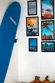agadir morocco surf setup with a cobalt-blue surfboard leaning against a white wall and a collage of travel prints above terracotta succulents